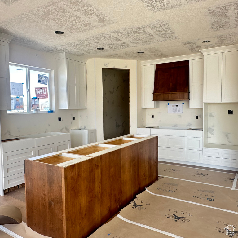 Kitchen with hardwood / wood-style floors, a textured ceiling, premium range hood, and white cabinetry