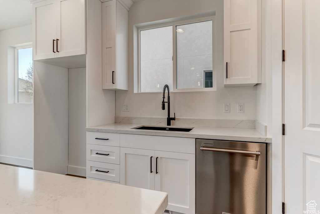 Kitchen with white cabinetry, stainless steel dishwasher, light stone countertops, and sink