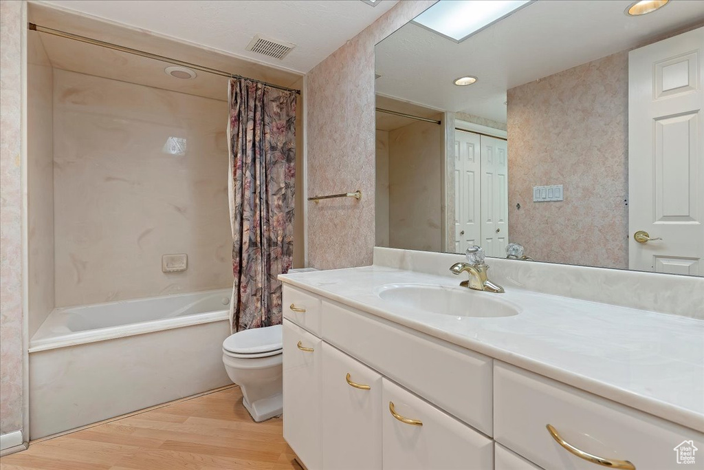 Full bathroom with hardwood / wood-style floors, toilet, vanity with extensive cabinet space, and shower / bath combo with shower curtain