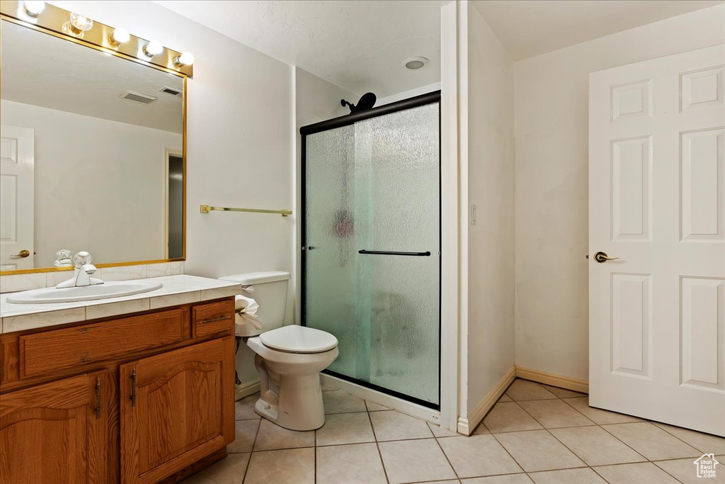 Bathroom featuring vanity, toilet, tile flooring, and a shower with door