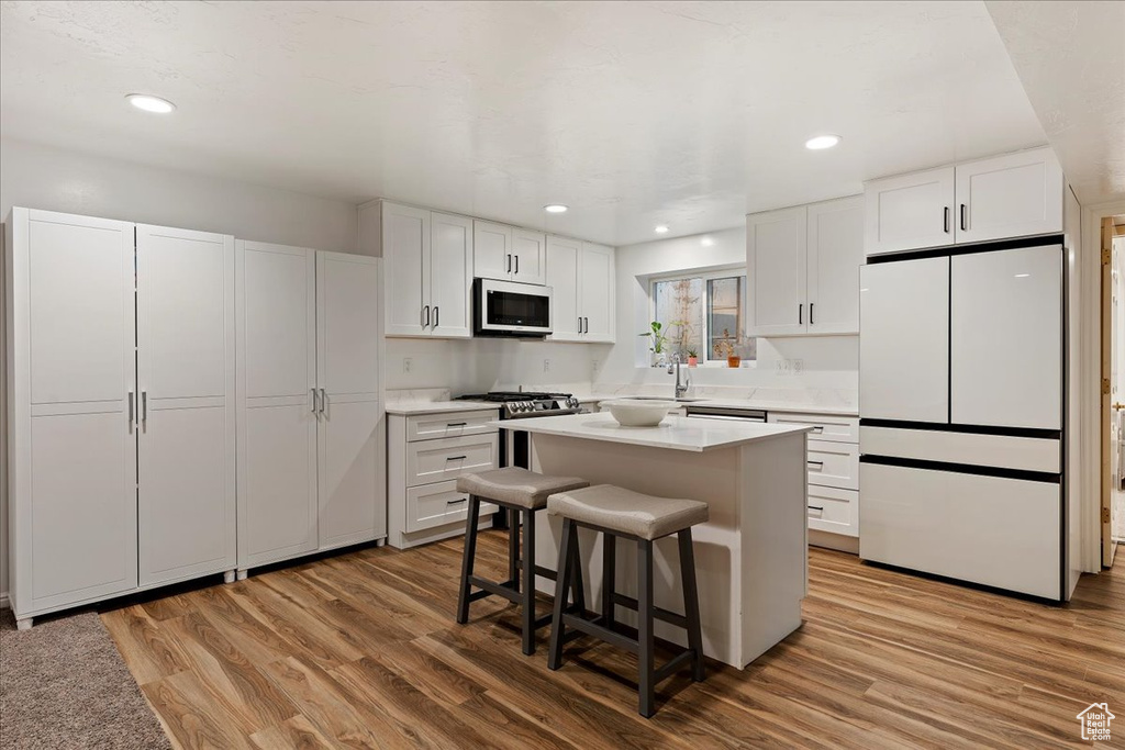 Kitchen with a kitchen breakfast bar, light wood-type flooring, appliances with stainless steel finishes, white cabinets, and a center island