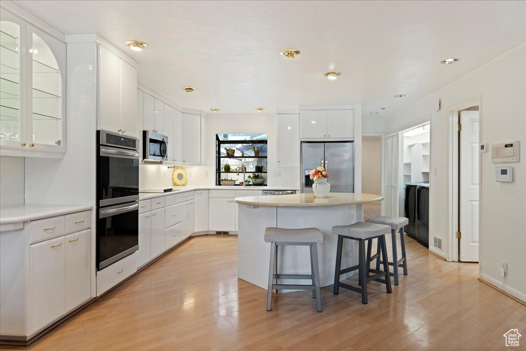 Kitchen with a kitchen island, a breakfast bar area, appliances with stainless steel finishes, light hardwood / wood-style flooring, and white cabinets