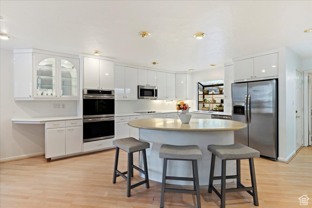 Kitchen featuring a breakfast bar, white cabinets, light wood-type flooring, and appliances with stainless steel finishes