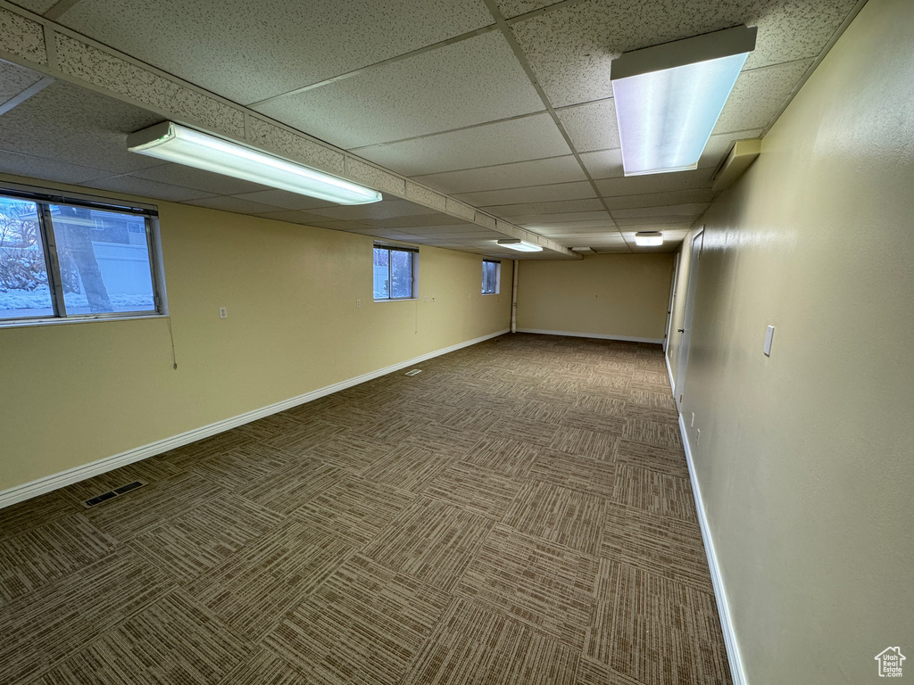 Interior space with a healthy amount of sunlight, a paneled ceiling, and dark carpet