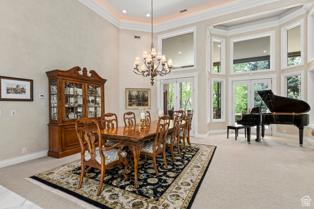 Carpeted dining area with crown molding, a high ceiling, french doors, and an inviting chandelier