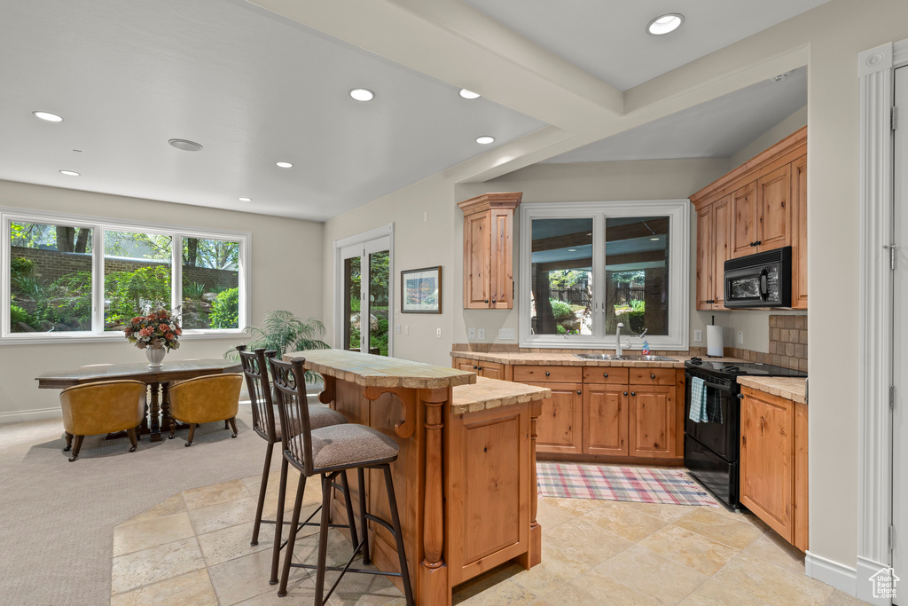 Kitchen with a breakfast bar, light tile flooring, electric stove, sink, and a center island