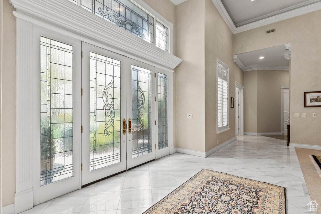Doorway to outside with ornamental molding, french doors, a towering ceiling, and light tile floors