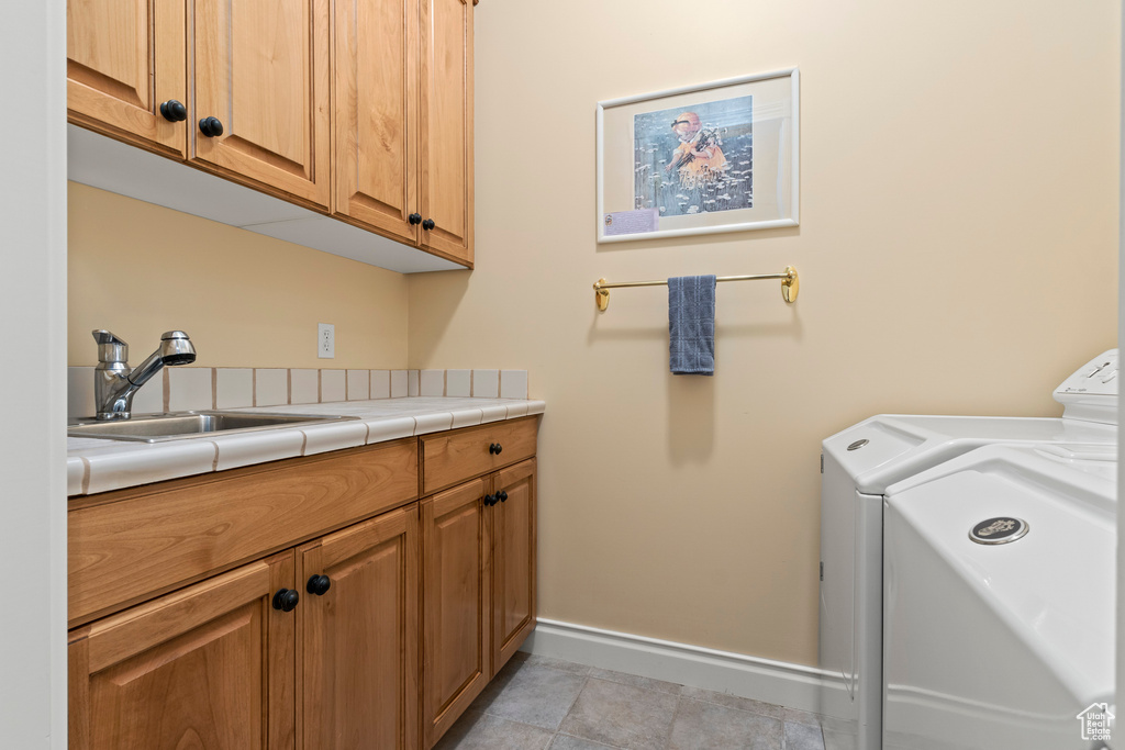 Laundry area with washing machine and clothes dryer, cabinets, light tile floors, and sink