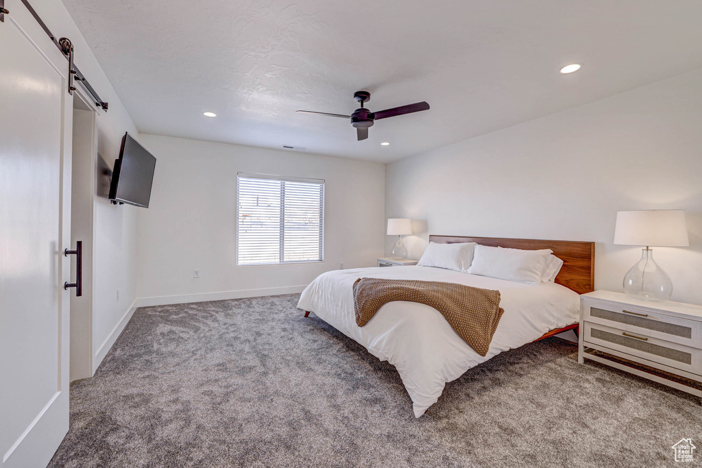 Carpeted bedroom with a barn door and ceiling fan