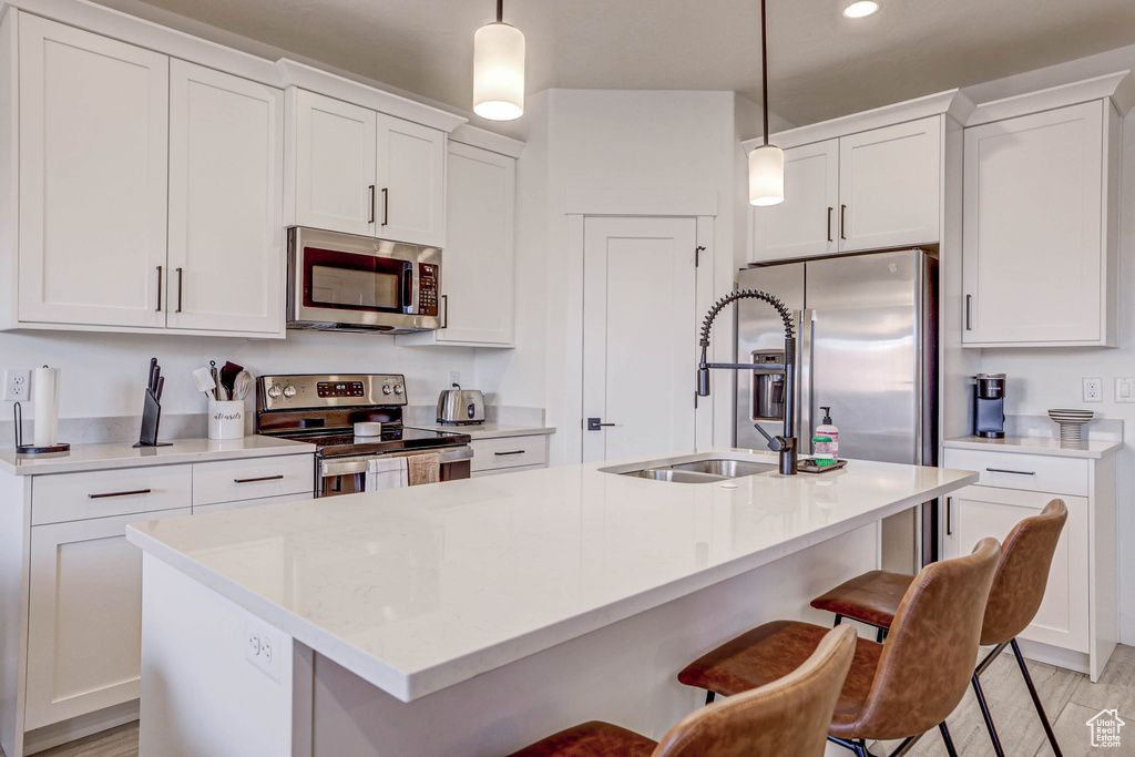 Kitchen featuring a kitchen bar, appliances with stainless steel finishes, pendant lighting, light wood-type flooring, and a kitchen island with sink