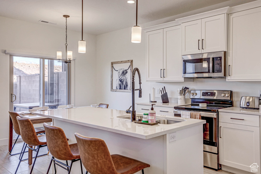 Kitchen featuring a breakfast bar, white cabinets, pendant lighting, stainless steel appliances, and a kitchen island with sink
