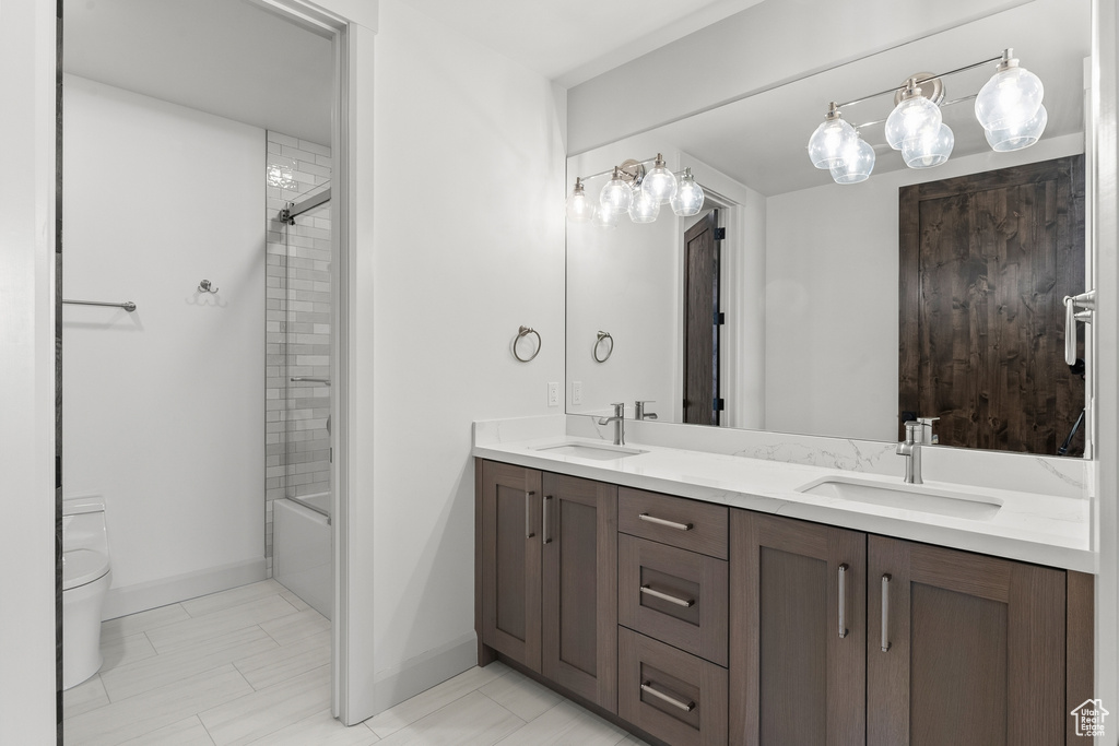 Full bathroom featuring vanity with extensive cabinet space, dual sinks, toilet, tile flooring, and tiled shower / bath