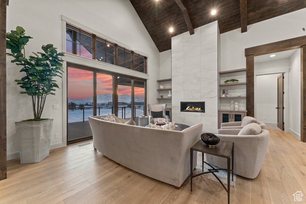 Living room with a water view, light hardwood / wood-style flooring, wooden ceiling, high vaulted ceiling, and a tile fireplace