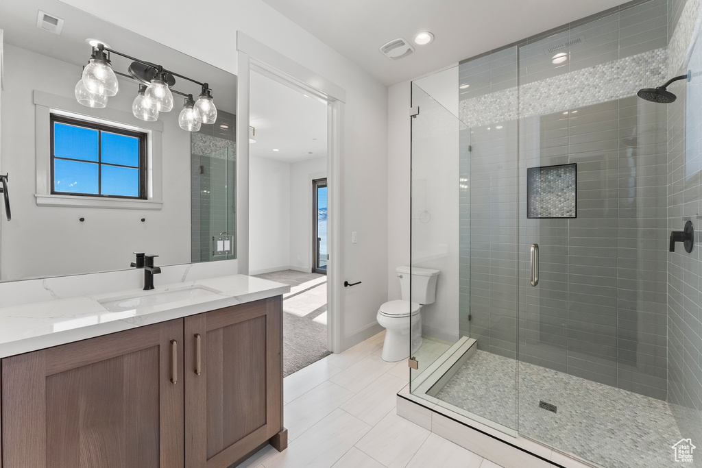 Bathroom featuring a shower with shower door, tile flooring, vanity, and toilet