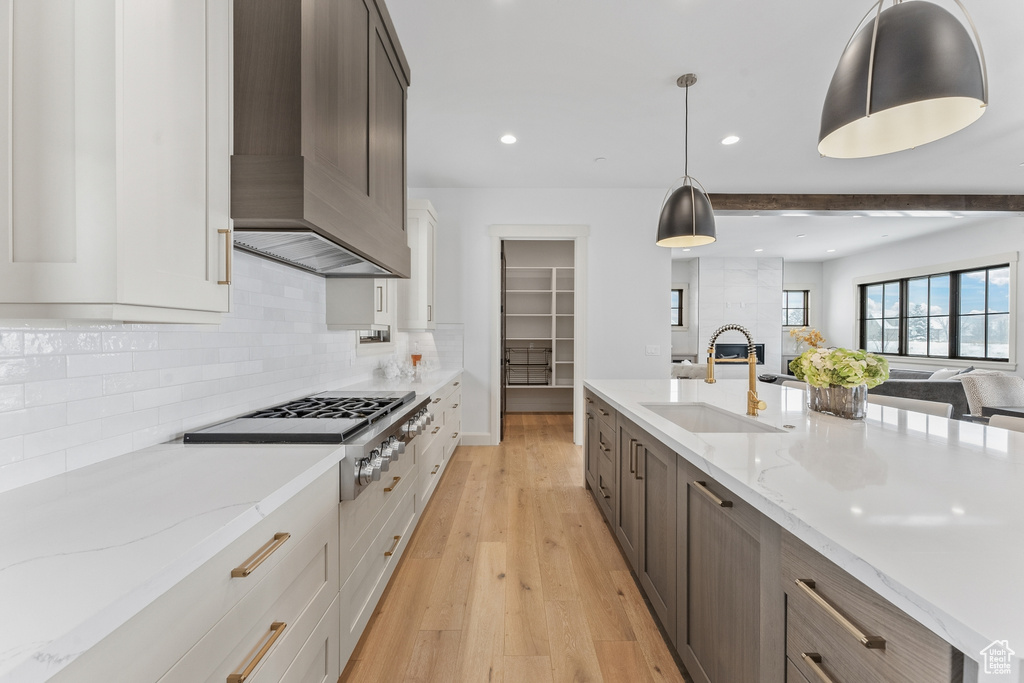 Kitchen with decorative light fixtures, light wood-type flooring, sink, tasteful backsplash, and white cabinetry