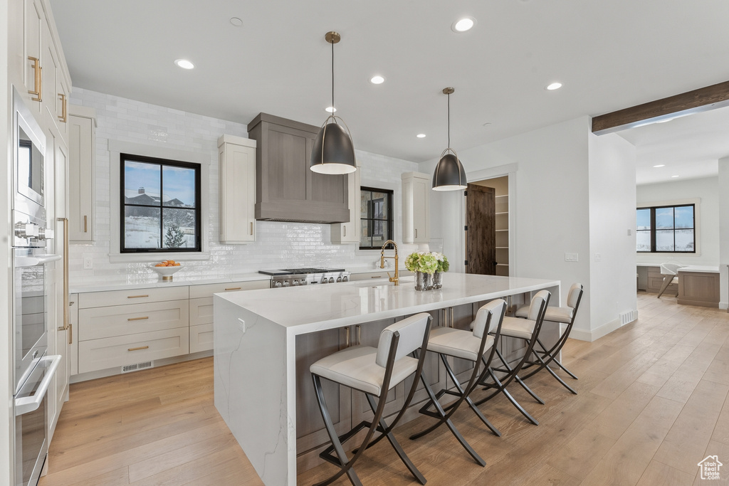 Kitchen with custom exhaust hood, a center island with sink, light wood-type flooring, pendant lighting, and a breakfast bar area