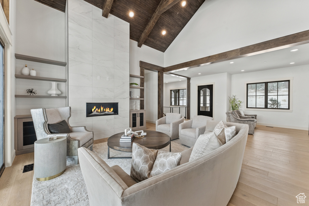 Living room with a tiled fireplace, light hardwood / wood-style floors, tile walls, and lofted ceiling with beams