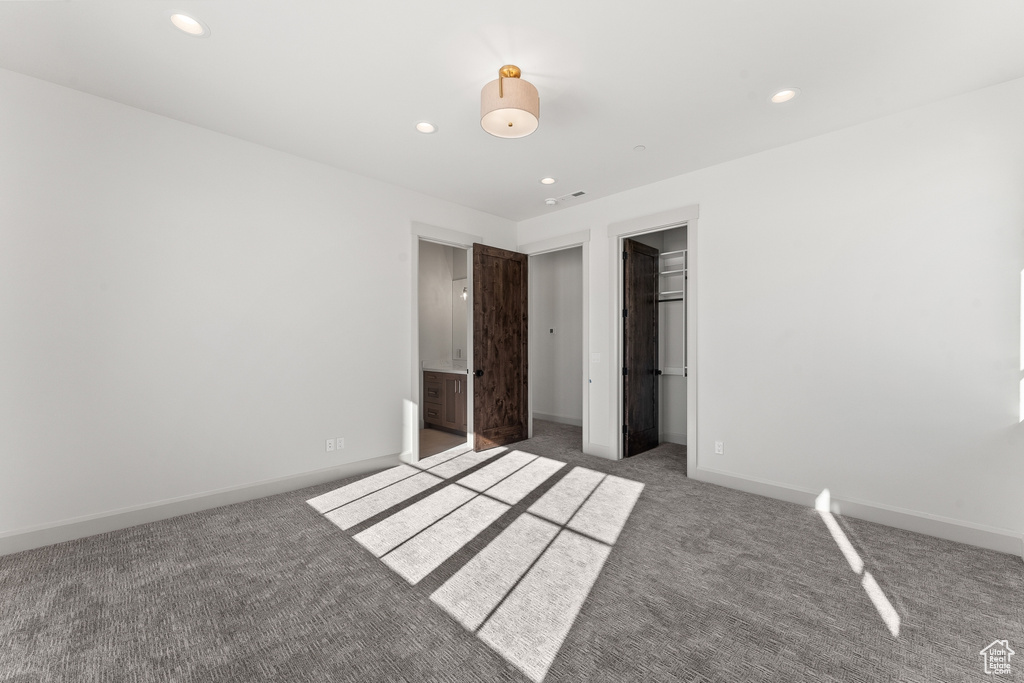 Unfurnished bedroom featuring a spacious closet, a closet, carpet floors, and ensuite bath