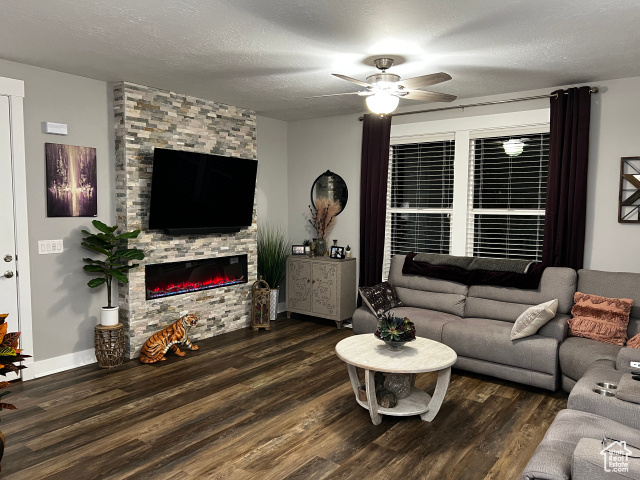 Living room with dark hardwood / wood-style flooring, a fireplace, a textured ceiling, and ceiling fan