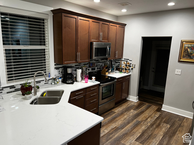 Kitchen featuring tasteful backsplash, dark hardwood / wood-style flooring, light stone counters, sink, and stainless steel appliances