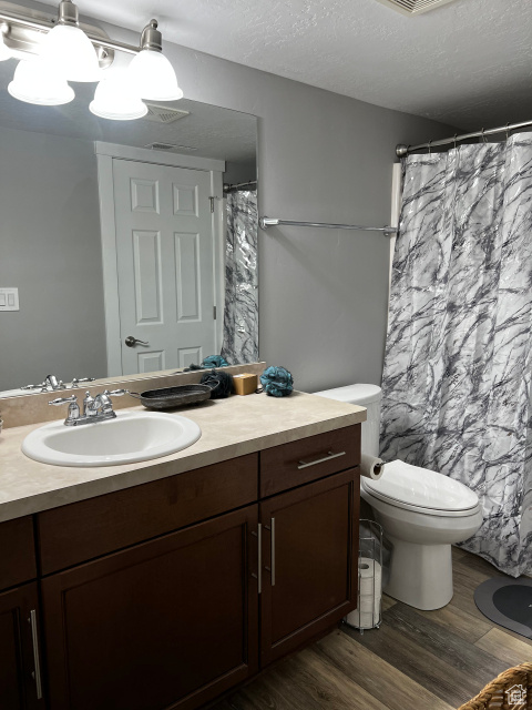 Bathroom with hardwood / wood-style floors, large vanity, toilet, and a textured ceiling