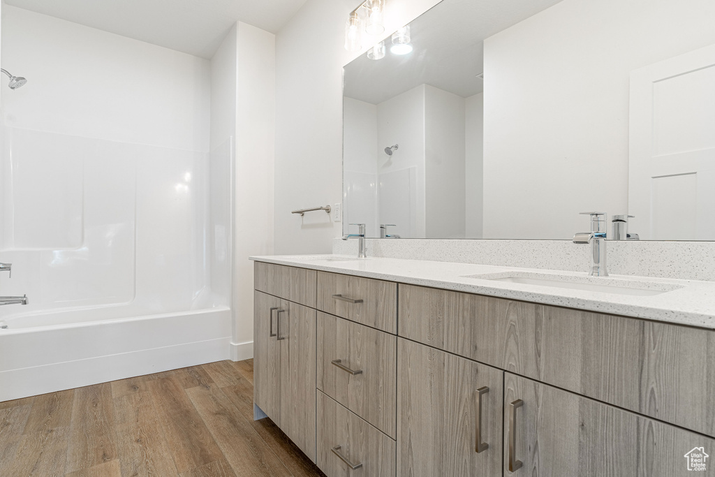Bathroom with hardwood / wood-style floors, vanity with extensive cabinet space, shower / washtub combination, and double sink