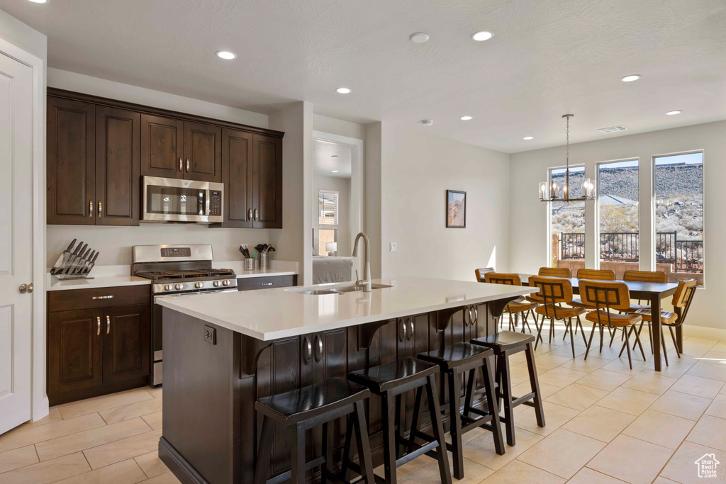 Kitchen featuring an inviting chandelier, pendant lighting, stainless steel appliances, an island with sink, and sink