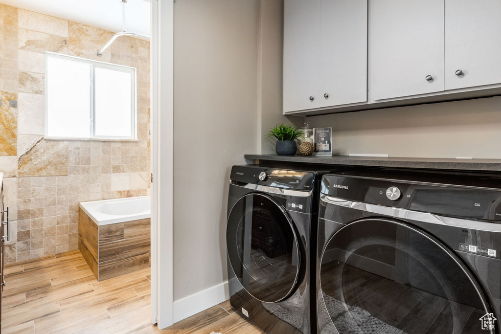 Laundry area featuring cabinets, separate washer and dryer, light hardwood / wood-style floors, and tile walls