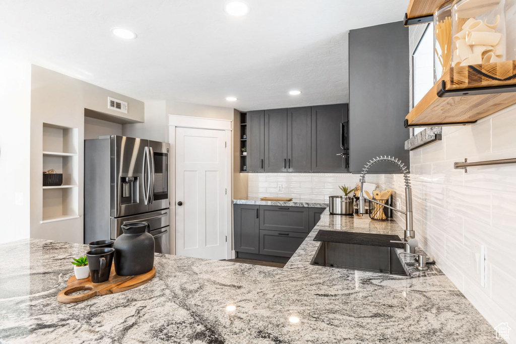 Kitchen featuring light stone countertops, gray cabinets, stainless steel fridge, backsplash, and sink