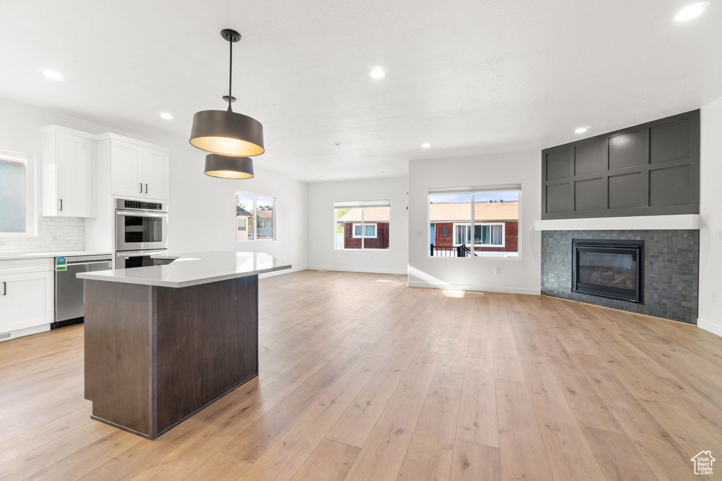 Kitchen featuring light hardwood / wood-style floors, a kitchen island, tasteful backsplash, hanging light fixtures, and appliances with stainless steel finishes