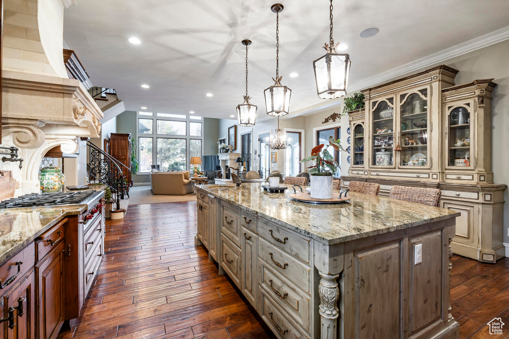 Kitchen with an inviting chandelier, dark hardwood / wood-style flooring, a center island with sink, and light stone counters