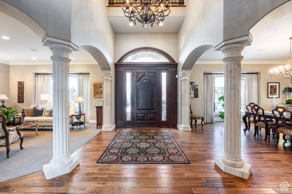 Entryway featuring an inviting chandelier, crown molding, ornate columns, and dark hardwood / wood-style flooring