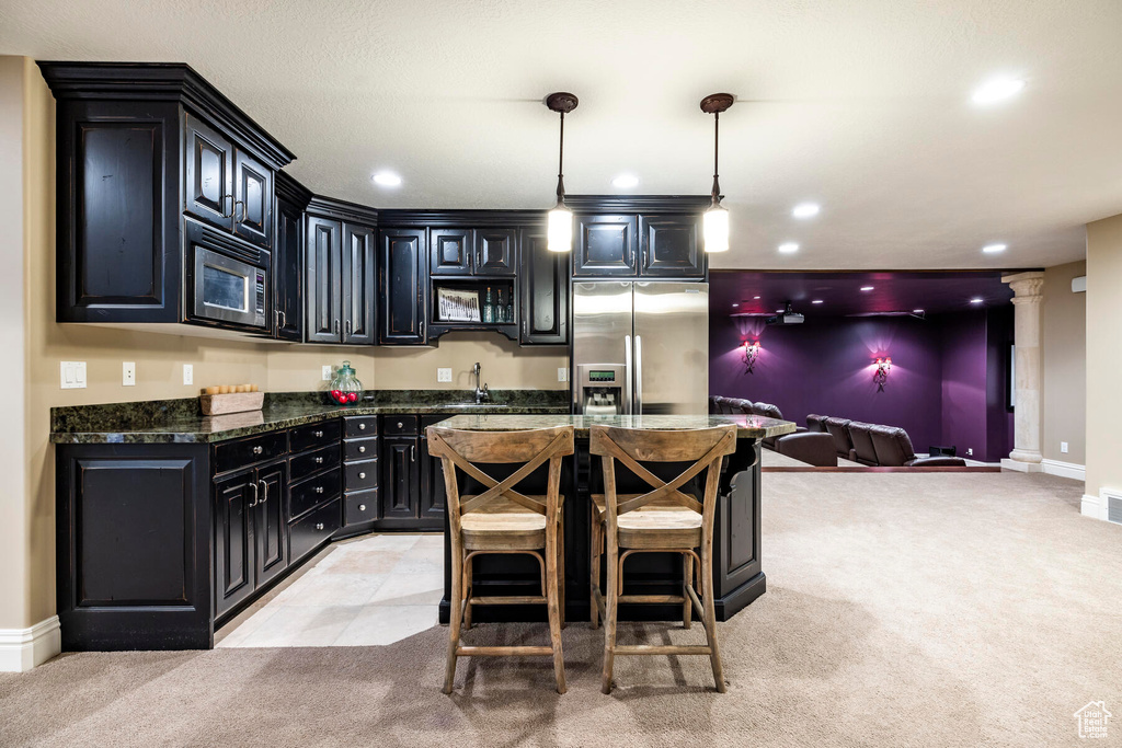 Kitchen with ornate columns, hanging light fixtures, light colored carpet, appliances with stainless steel finishes, and dark stone countertops