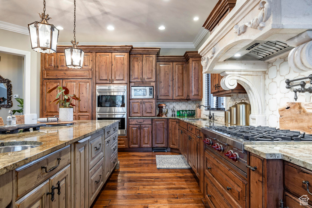 Kitchen with dark hardwood / wood-style flooring, appliances with stainless steel finishes, light stone countertops, and backsplash