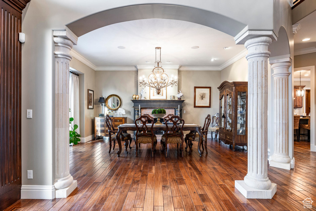Dining room featuring crown molding, a chandelier, ornate columns, and dark wood-type flooring