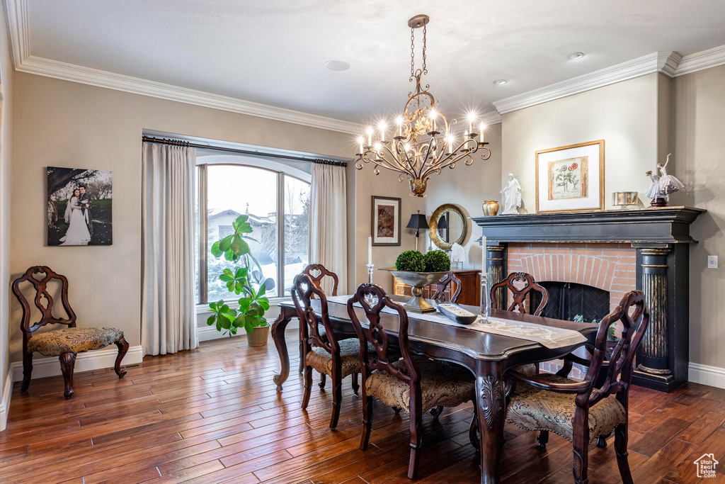 Dining room featuring a chandelier, dark hardwood / wood-style flooring, crown molding, and a brick fireplace