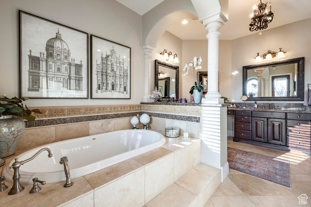 Bathroom with large vanity, tile floors, a notable chandelier, tiled bath, and decorative columns