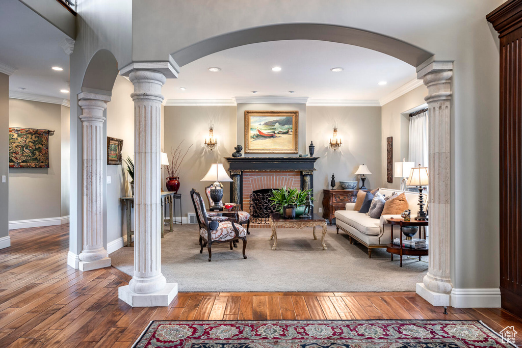 Carpeted living room with ornamental molding, a fireplace, and decorative columns
