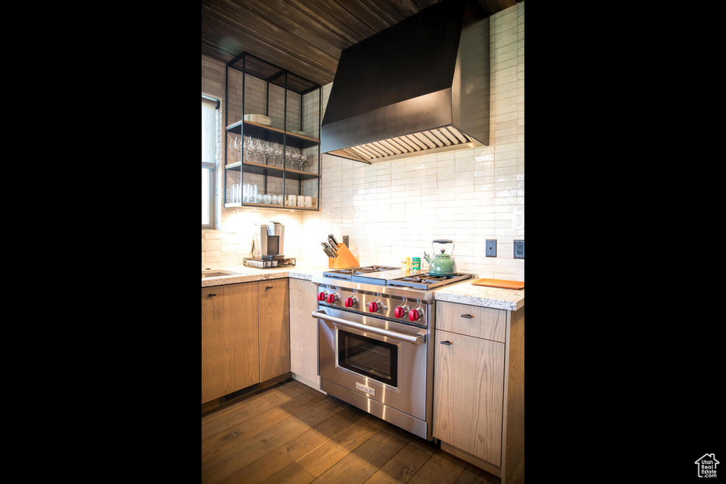 Kitchen with wall chimney exhaust hood, dark hardwood / wood-style flooring, premium range, and backsplash