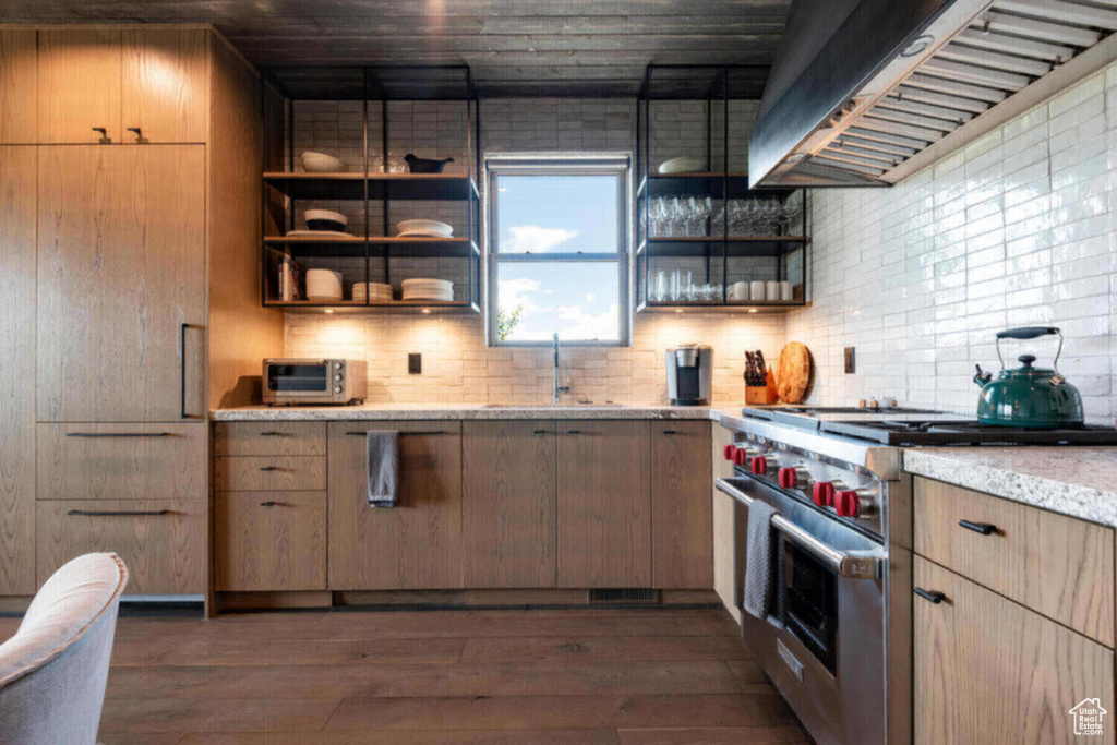 Kitchen with light stone counters, dark wood-type flooring, backsplash, luxury stove, and sink