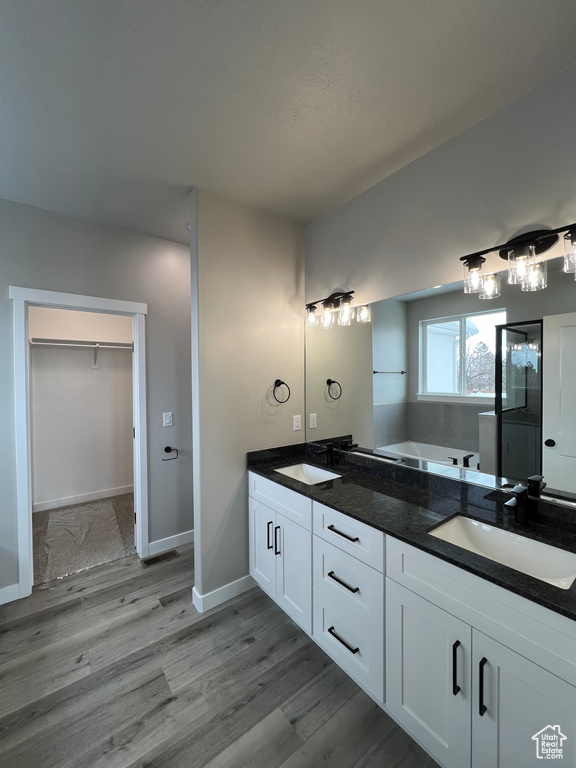 Bathroom featuring dual bowl vanity, a washtub, and hardwood / wood-style floors