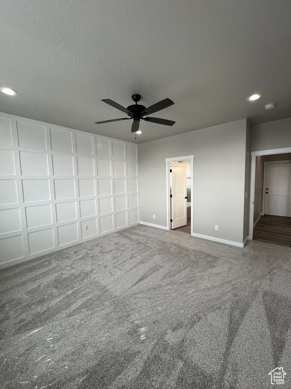 Unfurnished bedroom featuring ensuite bath, dark colored carpet, and ceiling fan
