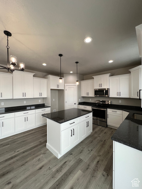 Kitchen with dark hardwood / wood-style flooring, appliances with stainless steel finishes, pendant lighting, and white cabinetry
