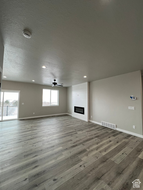 Spare room featuring dark hardwood / wood-style flooring, a large fireplace, a wealth of natural light, and ceiling fan