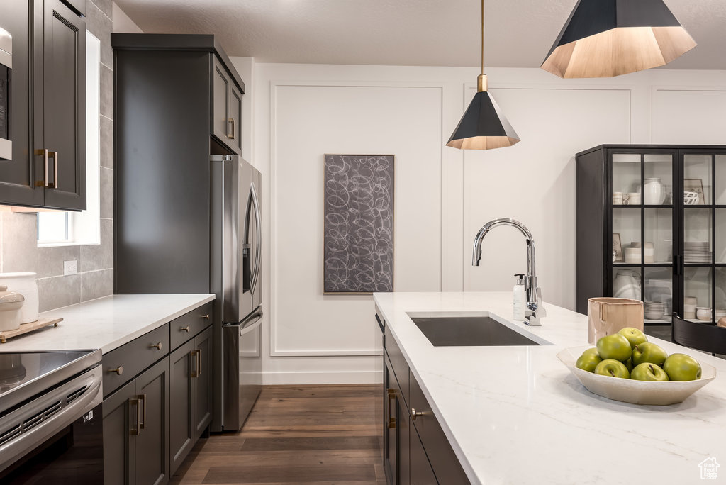 Kitchen with pendant lighting, stainless steel refrigerator with ice dispenser, backsplash, sink, and dark wood-type flooring