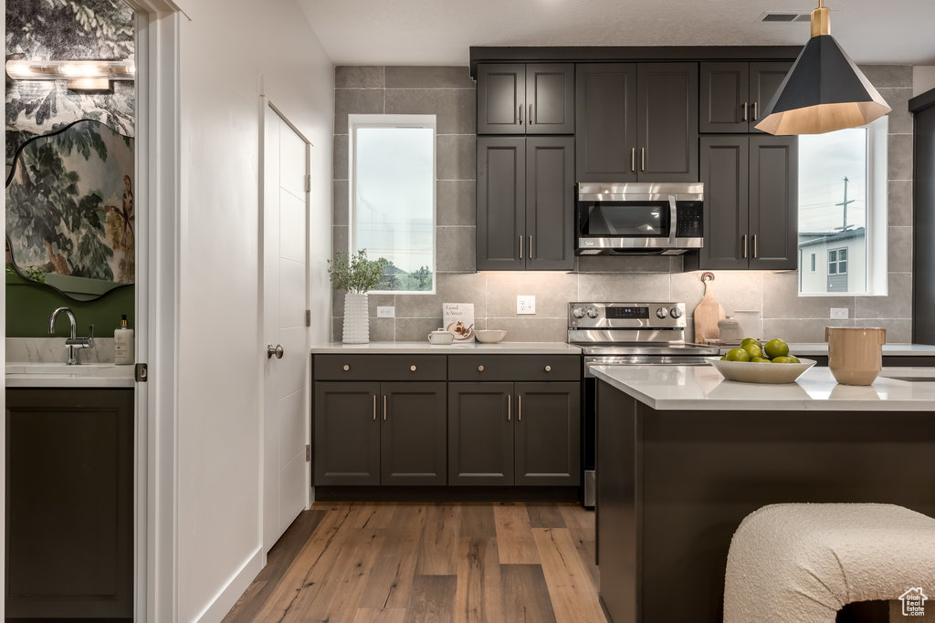 Kitchen with pendant lighting, gray cabinets, light wood-type flooring, backsplash, and sink