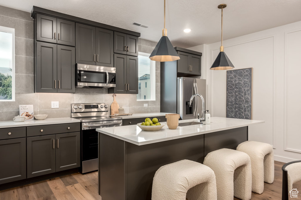 Kitchen featuring stainless steel appliances, light hardwood / wood-style flooring, pendant lighting, and a center island with sink