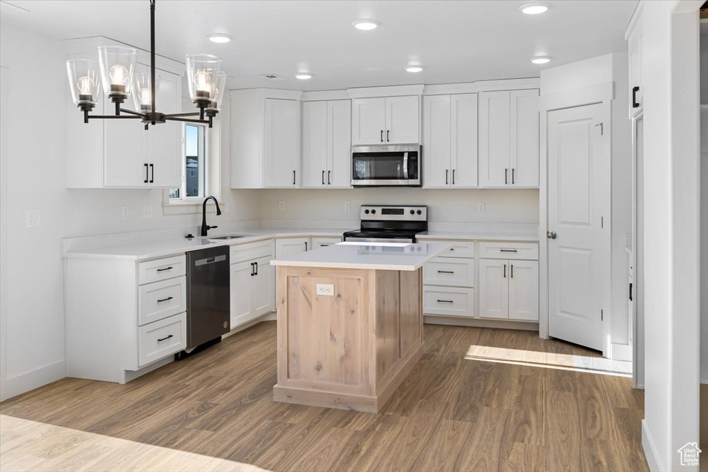 Kitchen featuring a kitchen island, white cabinetry, wood-type flooring, hanging light fixtures, and appliances with stainless steel finishes
