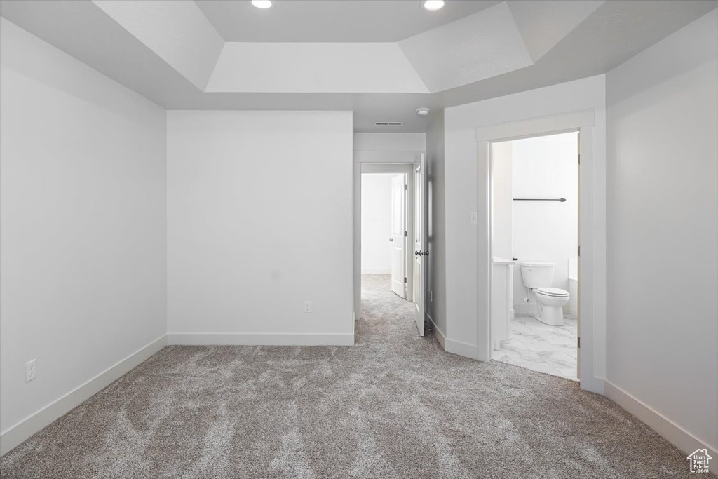 Unfurnished bedroom with connected bathroom, a tray ceiling, and light colored carpet