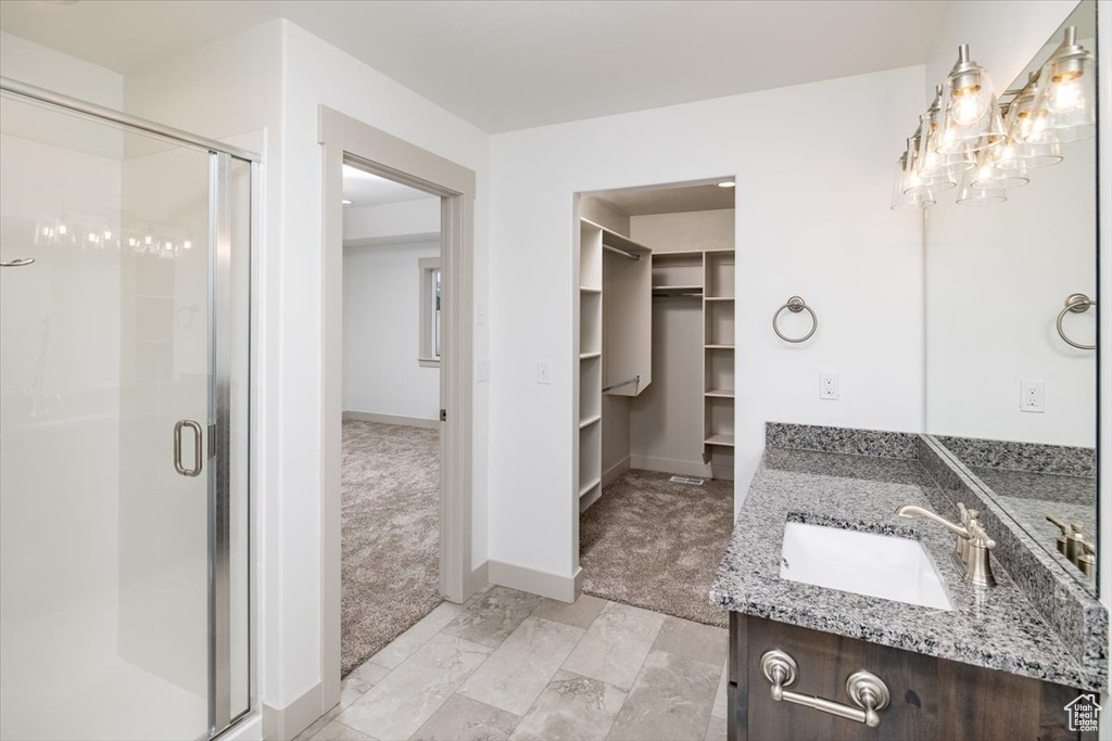 Bathroom with tile floors, a notable chandelier, vanity with extensive cabinet space, and walk in shower